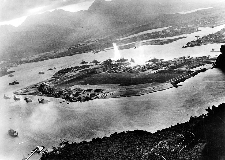 Black and white photograph of Pearl Harbor during the torpedo attack, from an aerial view from the Japanese planes.